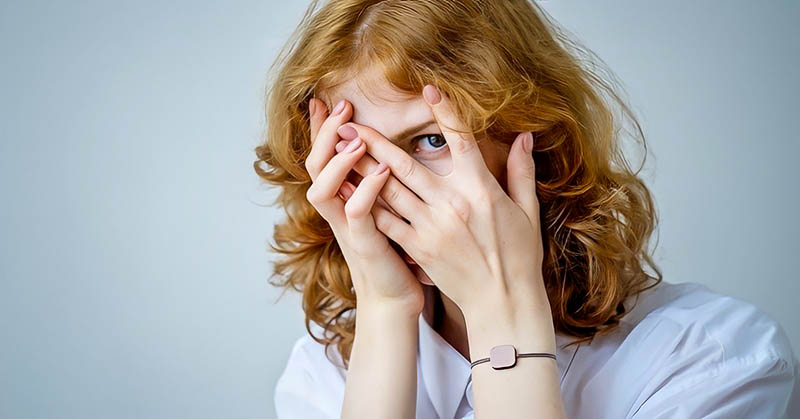 red-haired woman with eyes peeping through fingers illustrating a fear of being judged