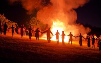 many people holding hands around a large bonfire