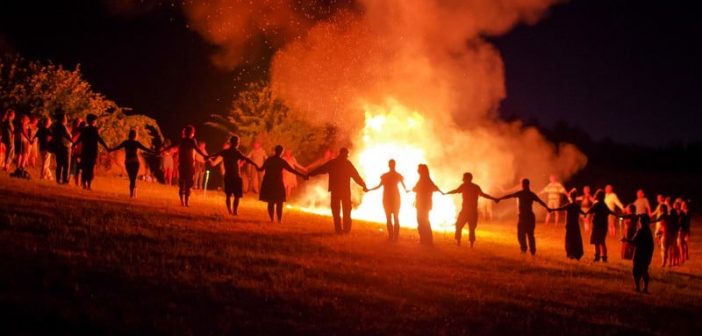 many people holding hands around a large bonfire