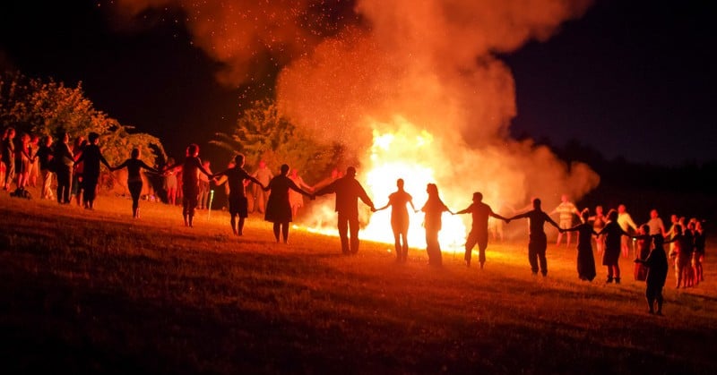 many people holding hands around a large bonfire