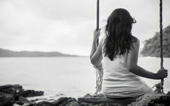 black and white photo of a young woman sitting on a swing looking out to sea - illustrating not knowing who you are