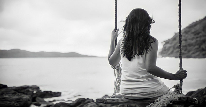 black and white photo of a young woman sitting on a swing looking out to sea - illustrating not knowing who you are