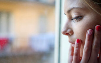 young woman looking out of window and worrying about the future