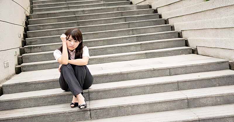 anxious young businesswoman sitting on some steps illustrating a fear of success