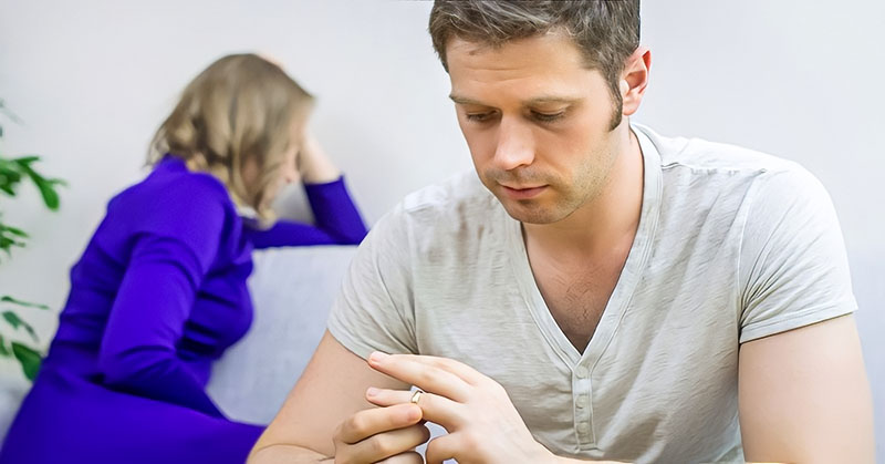 a husband taking his ring off with sad wife in the background illustrating him leaving her