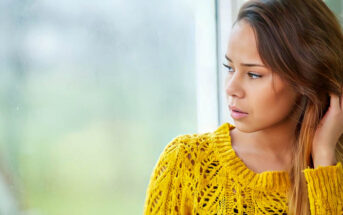 pensive young woman looking out of a window, wondering whether she is wasting her life