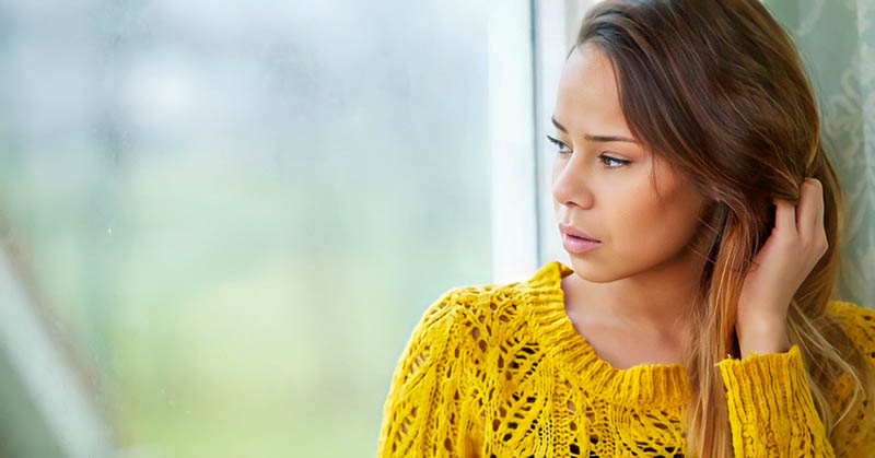 pensive young woman looking out of a window, wondering whether she is wasting her life