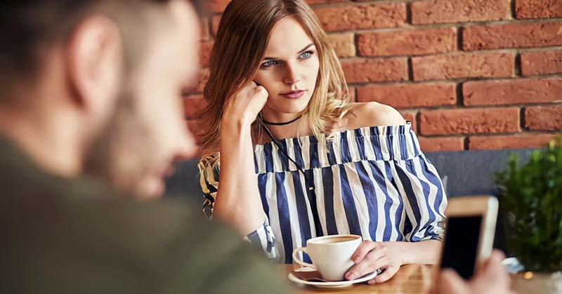 girl looking sad opposite guy who's on his phone - illustrating that he is keeping her around but not interested in a relationship