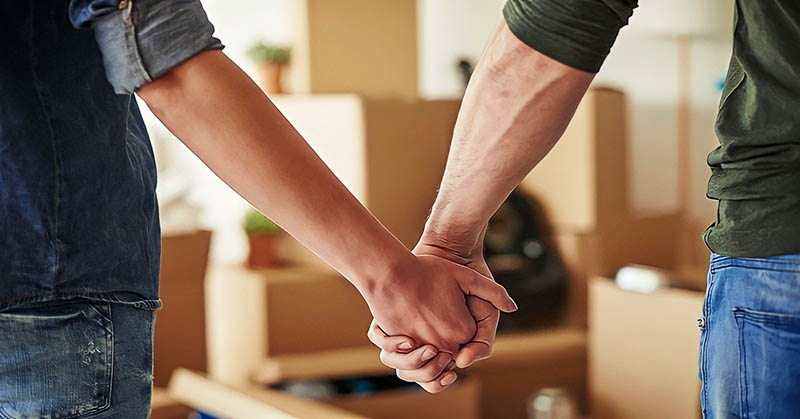 a couple holding hands after moving in together with cardboard boxes in the background