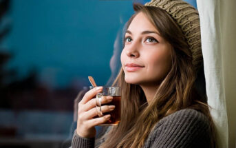 smiling thoughtful woman holding a hot drink - illustrating being the best version of yourself