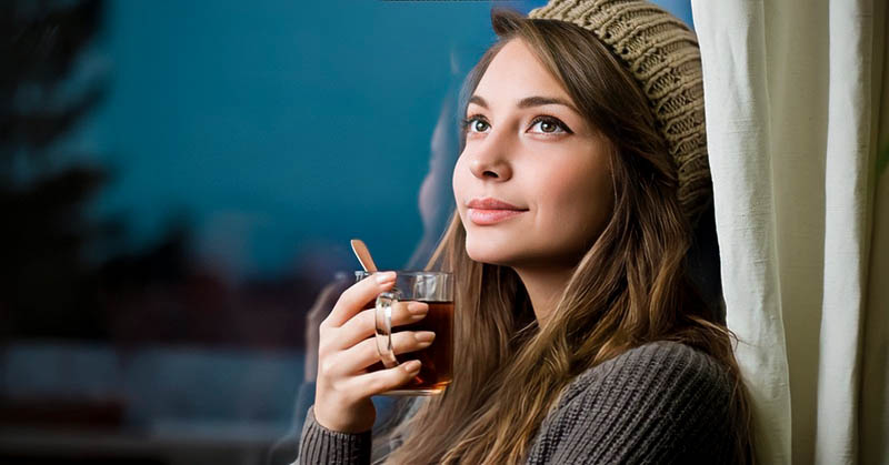 smiling thoughtful woman holding a hot drink - illustrating being the best version of yourself