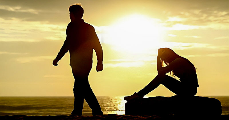 silhouette of man walking away from woman against setting sun - illustrating ending an affair