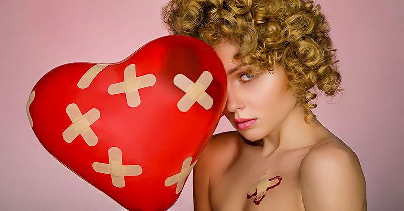 woman holding heart balloon with plasters all over it illustrating the pain and hurt of love