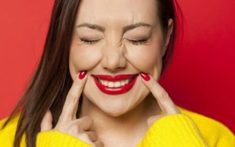 woman pushing sides of her mouth up to form a smile - illustrating toxic positivity