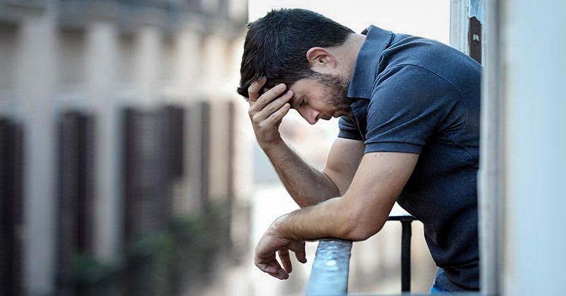 young man on balcony with hand on head illustrating the feeling of being a burden