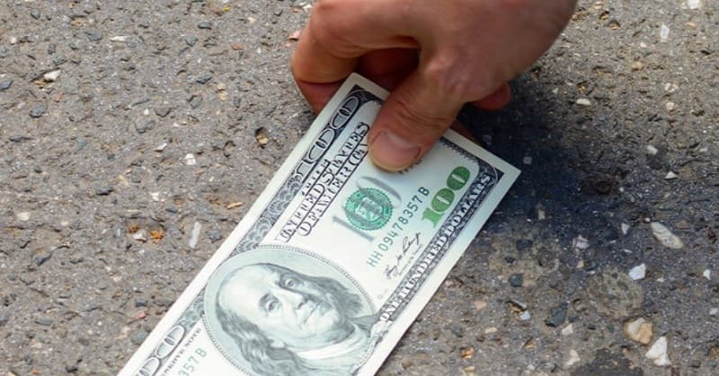 person finding a one hundred dollar bill on the ground - illustrating good luck