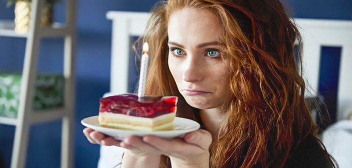 sad woman staring at candle on slice of cake illustrating that she hates her birthday