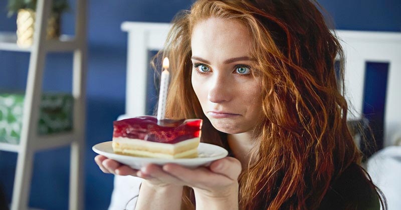 sad woman staring at candle on slice of cake illustrating that she hates her birthday