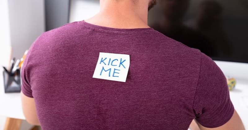 man with "kick me" note on his back illustrating public humiliation