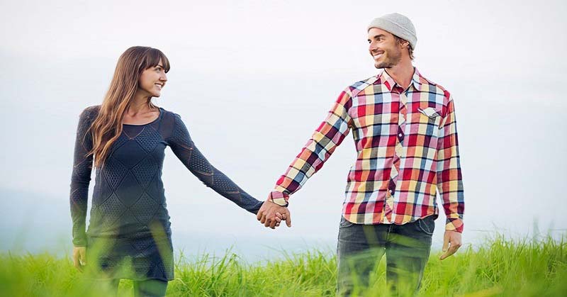 couple holding hands walking through grassy field illustrating patience in a relationship