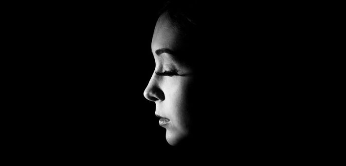 woman looking sad with closed eyes against a dark background to illustrate toxic shame
