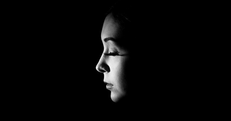 woman looking sad with closed eyes against a dark background to illustrate toxic shame