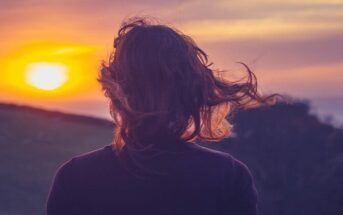 young woman looking out at the sunset with hair blowing in the wind
