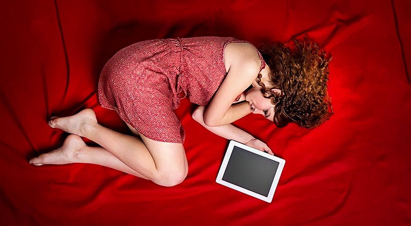 sad woman curled up on bed next to tablet signifying a long-distance breakup