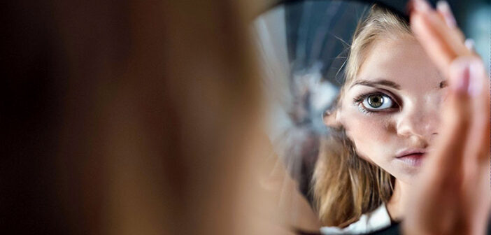 young woman looking at herself in broken mirror thinking that she doesn't deserve love