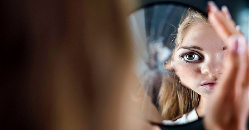 young woman looking at herself in broken mirror thinking that she doesn't deserve love