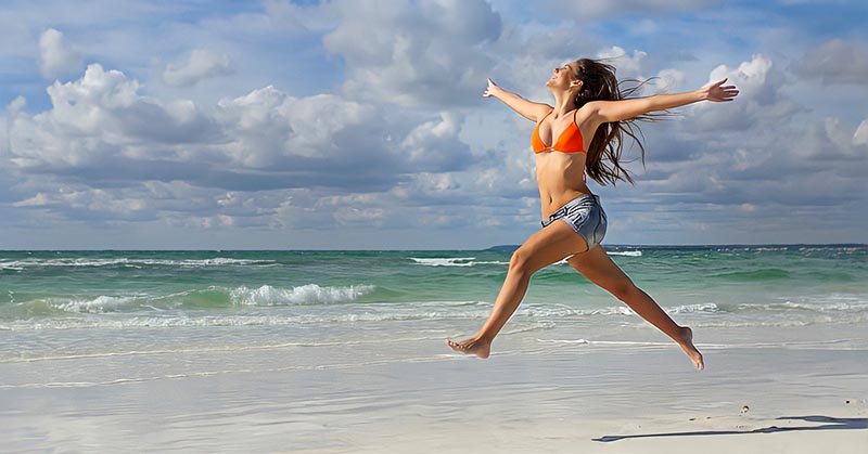 woman jumping up and celebrating on a beach illustrating winning at life
