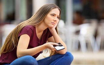 woman holding phone looking sad trying to decide whether she should block her ex