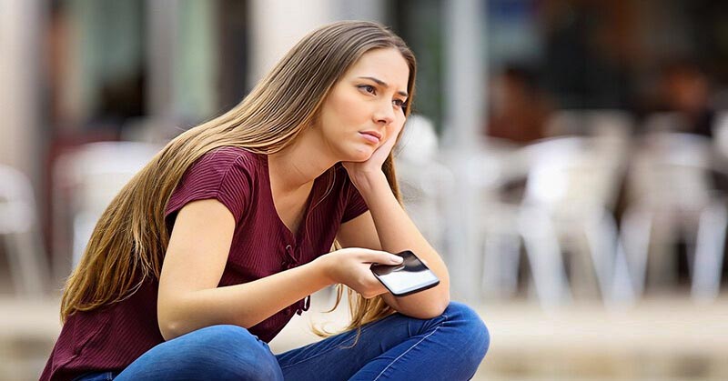 woman holding phone looking sad trying to decide whether she should block her ex