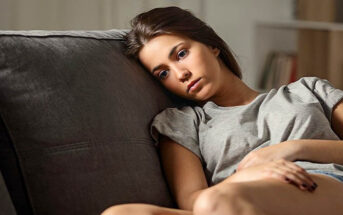 young woman sitting on couch looking sad because she can't stop thinking about a guy