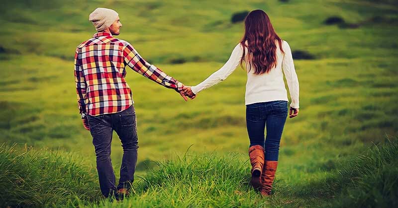 couple holding hands walking through field to illustrate companionship in a relationship