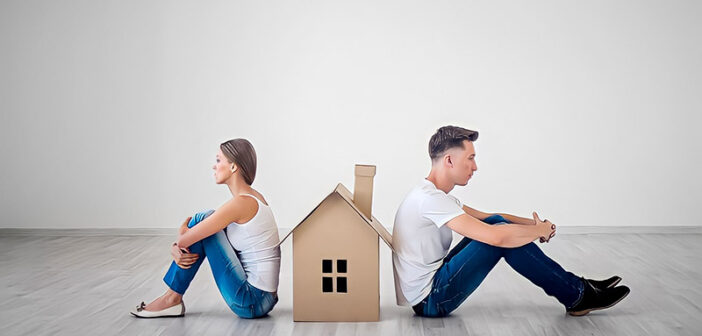 couple sitting facing away from each other with cardboard house between them - illustrating an in-house trial separation