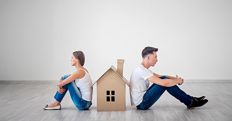 couple sitting facing away from each other with cardboard house between them - illustrating an in-house trial separation