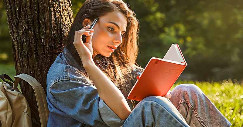 woman sitting under a tree writing her life purpose statement in a notepad