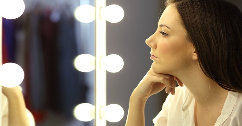 woman looking at her reflection in a mirror to illustrate self-reflection questions
