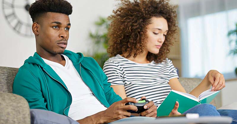 selfish husband playing computer games whilst his wife looks at book