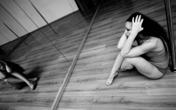 woman in dance studio sitting on floor looking sad - illustrating trying to stay positive in a negative world