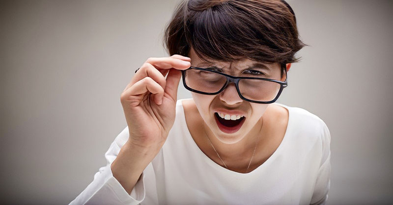 woman with scrunched up face holding her glasses looking very critical of others