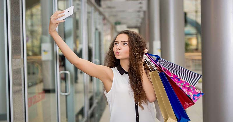 young woman taking selfie with shopping bags whilst pouting - signs of a try hard