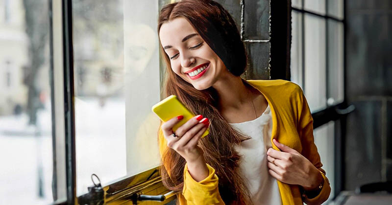 smiling woman looking at phone - illustrating texting too much before a first date