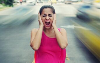 woman screaming holding her ears as traffic drives past - illustrating a world that is going crazy