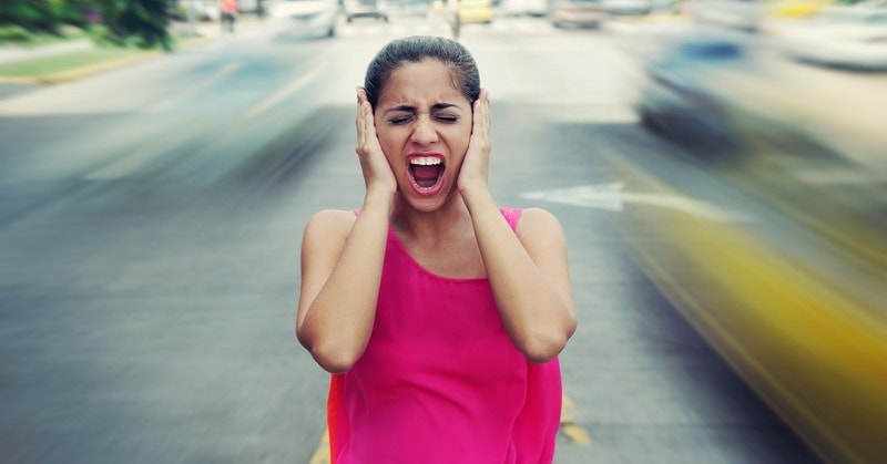 woman screaming holding her ears as traffic drives past - illustrating a world that is going crazy