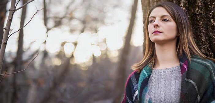 pensive looking woman standing in a forest thinking she needs a change in life