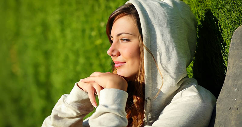 a young woman sitting with face toward the sun with a little smile on her face after rebooting her life