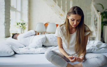 worried girl sitting on bed with boyfriend in the background wondering why he doesn't love her