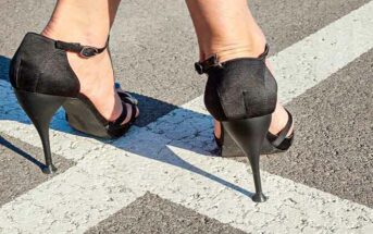 closeup of woman's feet in high heels standing on white lines going in opposite directions - illustrating a crossroads in life